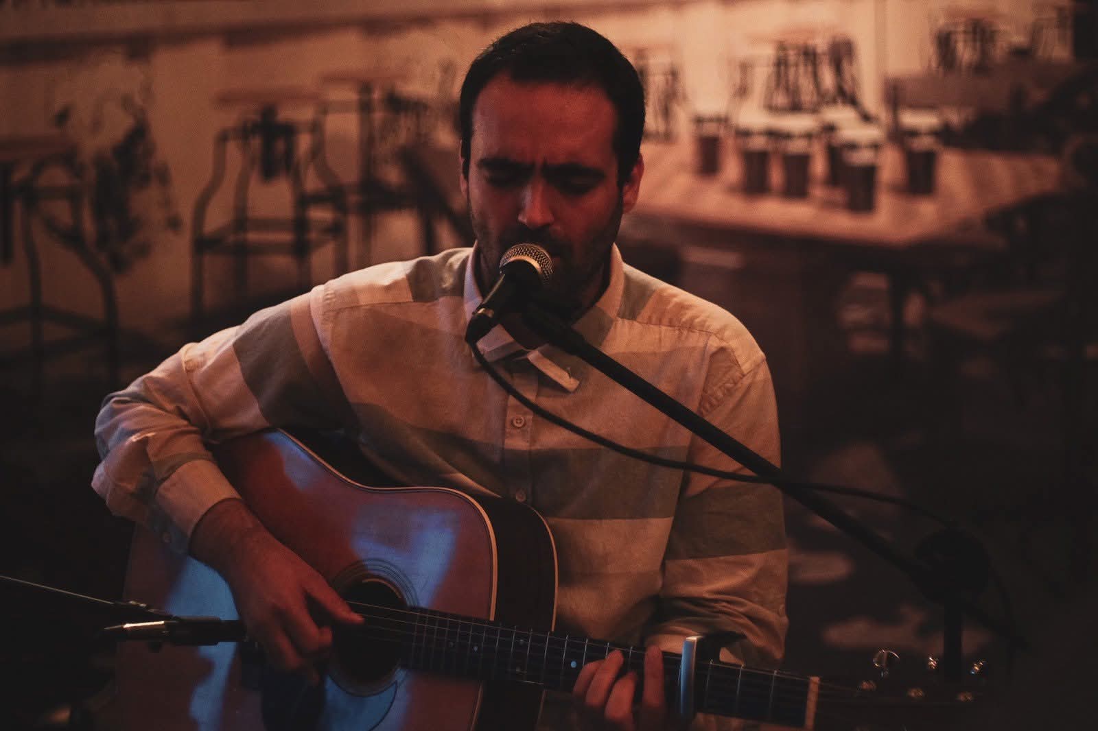 Ilko Birov singing and playing acoustic guitar in warm stage light in Plovdiv