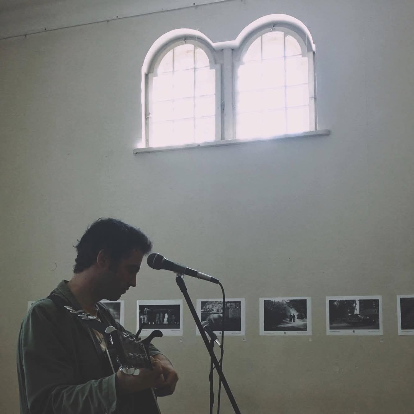 Ilko Birov performing guitar in a quiet gallery beneath arched windows